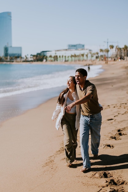 Um casal alegre correndo de mãos dadas ao longo de uma praia ensolarada em Barcelona, Espanha