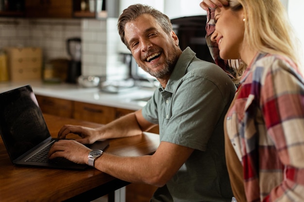 Foto um casal alegre desfruta de um momento alegre em sua cozinha ensolarada trabalhando em um laptop cercado por um pequeno-almoço saudável