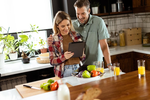 Um casal alegre está em uma cozinha bem iluminada absorvido em um tablet digital entre ingredientes frescos