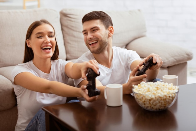 Um casal alegre jogando videogame sentado no sofá em casa