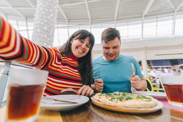 Foto um casal alegre sentado num café a comer pizza com fome.