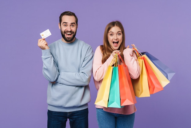 um casal amoroso animado feliz positivo isolado na parede roxa, segurando sacolas de compras e cartão de crédito.
