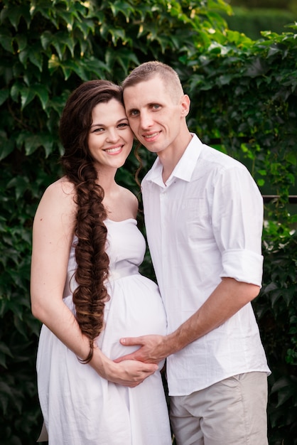 Um casal amoroso grávida abraça em um parque de verão e sorrisos