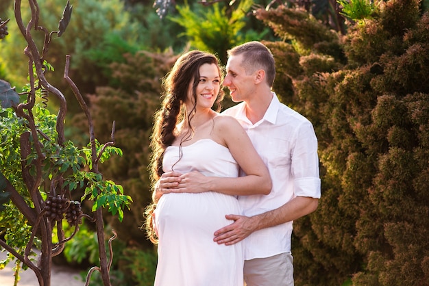 Um casal amoroso grávida abraça em um parque de verão e sorrisos