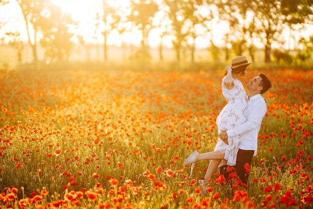 Um casal apaixonado no campo de papoulas ao pôr-do-sol a desfrutar do tempo juntos, do amor e do estilo de vida.