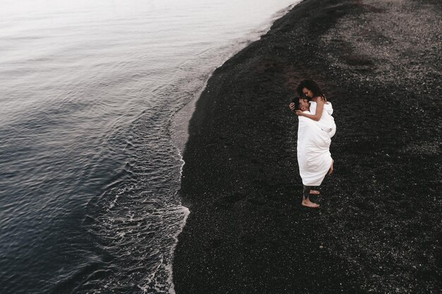 Foto um casal apaixonado passa a noite no mar a beijar-se e a abraçar-se na praia coberto por um cobertor.