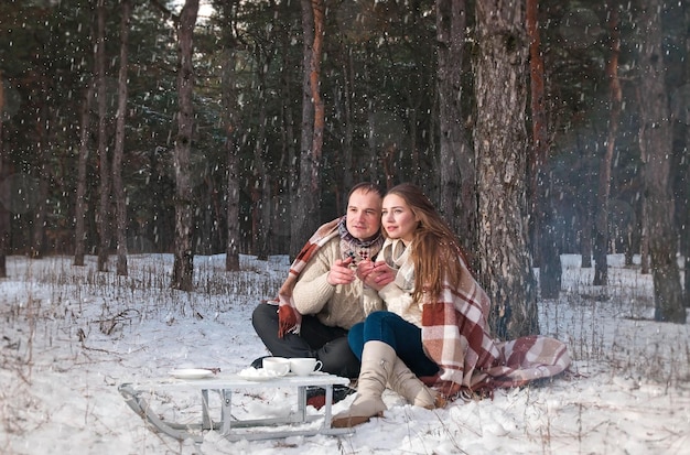 um casal apaixonado senta-se na floresta no inverno, relaxa em um cobertor com chá