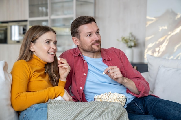 Um casal apaixonado sentado confortavelmente no sofá a desfrutar de ver um filme. Homem e mulher a passar um fim-de-semana preguiçosos.