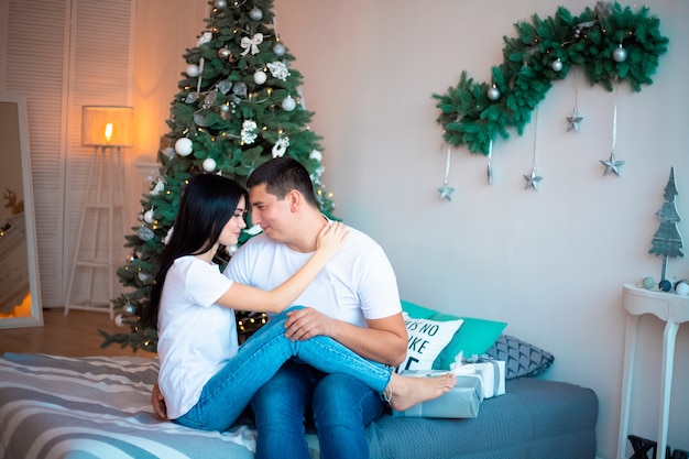 Um casal apaixonado, sentado em uma cama em um quarto decorado com enfeites de Natal.