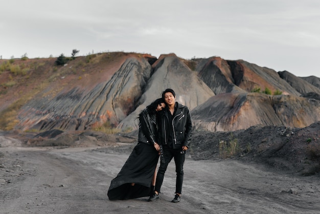 Um casal asiático apaixonado por roupas de couro preto caminha pela natureza entre as árvores. Estilo, moda, amor