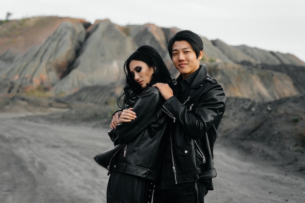 Um casal asiático apaixonado por roupas de couro preto caminha pela natureza entre as árvores. Estilo, moda, amor