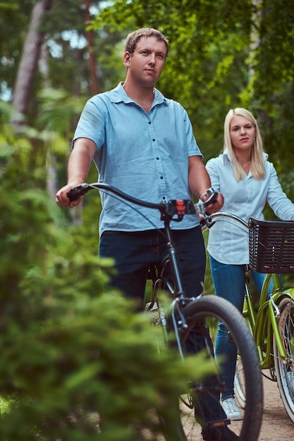 Um casal atraente de uma mulher loira e um homem vestido com roupas casuais em um passeio de bicicleta em um parque.