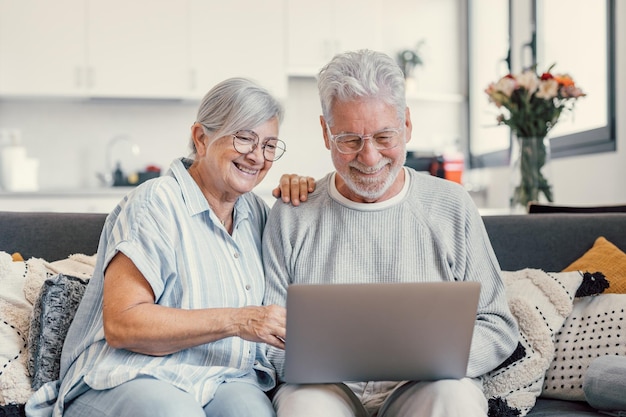 Um casal bem idoso de 70 anos de cabelos grisalhos descansando no sofá na sala de estar segurando um laptop assistindo a um filme sorrindo desfrutando do tempo livre geração mais velha e tecnologia sem fio moderna usuários avançados conceptxA