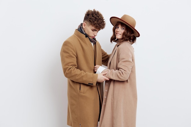 Foto um casal bonito está de pé de lado em um fundo claro vestido com casacos e camisolas abraçando as mãos um do outro