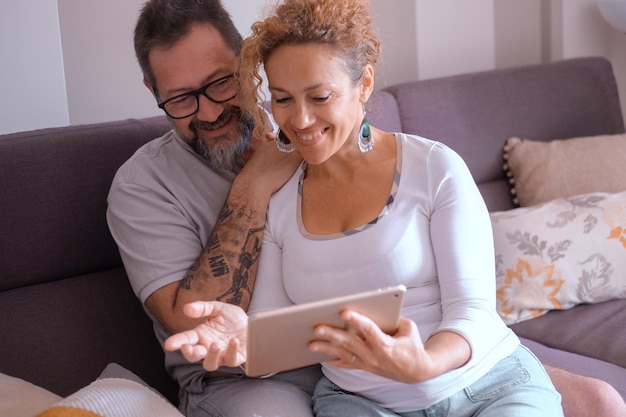 Um casal caucasiano maduro feliz sentado no sofá de casa usando um tablet digital navegando na rede