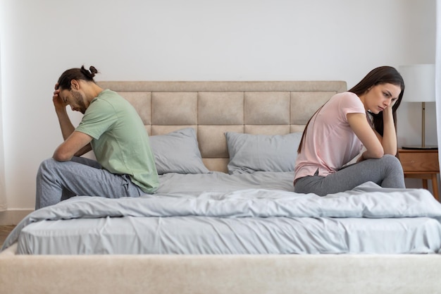 Um casal chateado sentado separadamente na cama de frente para o outro