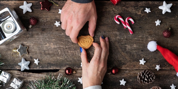 Um casal colocando biscoito de férias com a palavra amor sobre ele na mesa de madeira rústica cheia de decorações de Natal.
