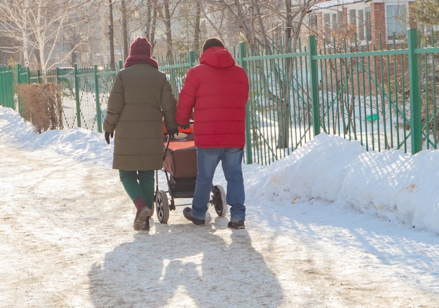 Um casal com um carrinho de bebê caminha pelo parque de inverno durante uma caminhada Tempo nevado