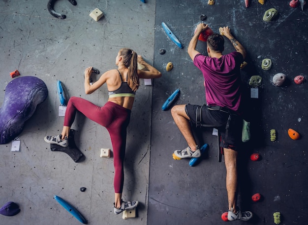 Um casal de alpinistas fortes escala uma parede artificial com garras e cordas coloridas