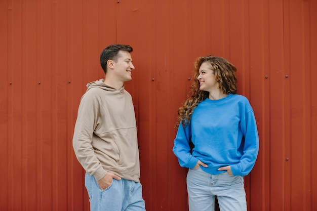 Foto um casal de amigos, um menino e uma menina estão falando no fundo de uma parede vermelha ao ar livre