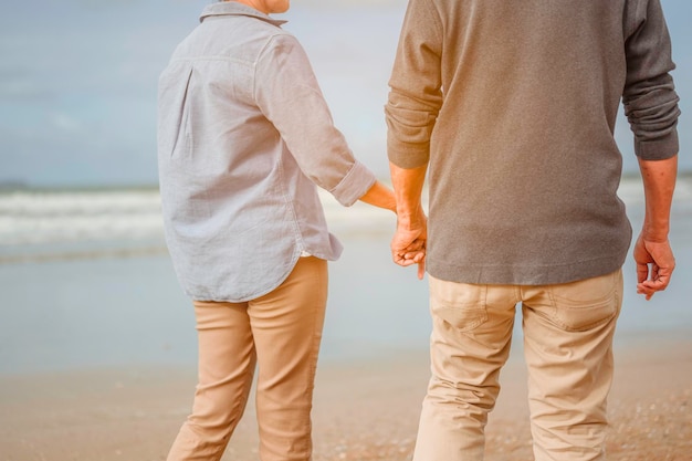 Um casal de aposentados anda de mãos dadas na praia ao nascer do sol, plano de seguro de vida no conceito de aposentadoria.