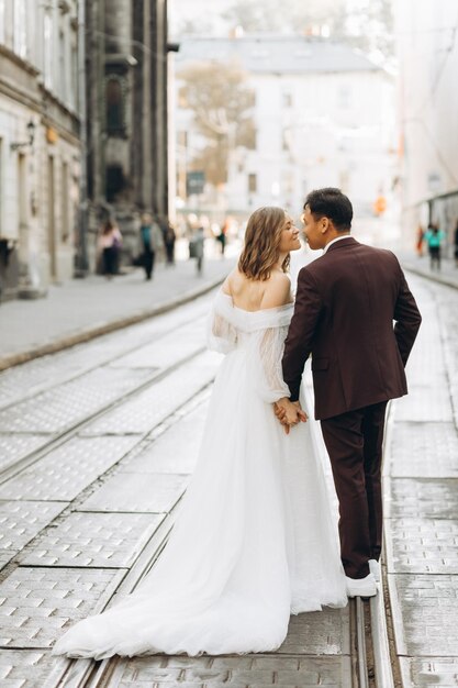 Um casal de casamento internacional, uma noiva europeia e um noivo asiático andam juntos pela cidade