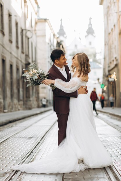 Um casal de casamento internacional, uma noiva europeia e um noivo asiático andam juntos pela cidade