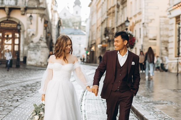 Um casal de casamento internacional, uma noiva europeia e um noivo asiático andam juntos pela cidade