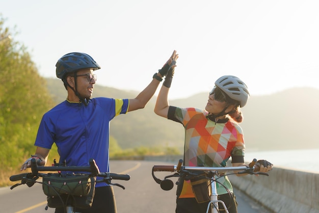 Um casal de ciclistas asiáticos fazem highfive juntos depois de andar de bicicleta até o seu destino ao redor de um lago