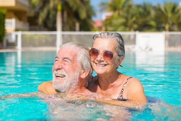 Um casal de dois idosos felizes a divertir-se e a desfrutar juntos na piscina a sorrir e a brincar pessoas felizes a gostar do verão ao ar livre na água