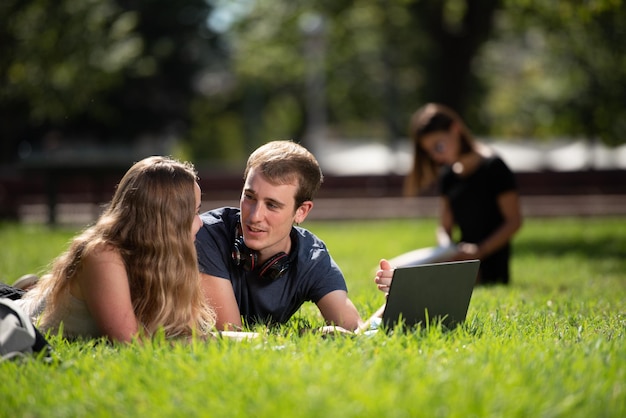 Um casal de estudantes universitários conversando deitados no chão do parque do campus