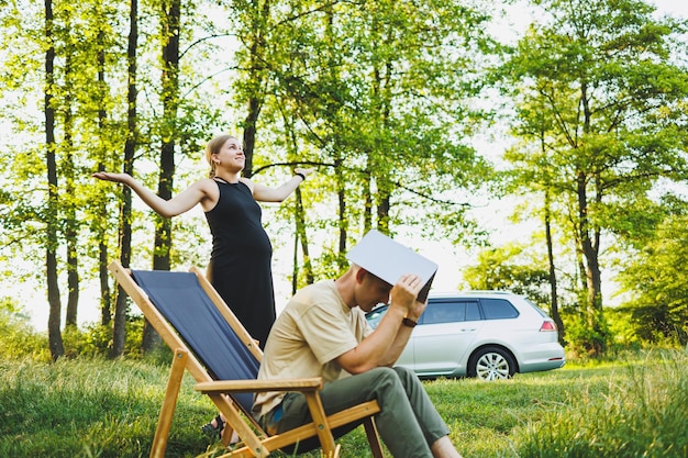 Um casal de família um homem e uma mulher estão relaxando na natureza e trabalhando remotamente com um laptop piquenique de casais apaixonados com trabalho on-line Uma mulher grávida descansa na natureza com seu marido