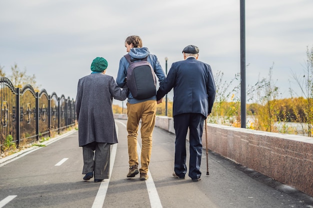 Um casal de idosos caminha no parque com um assistente masculino ou neto adulto Cuidando do voluntariado idoso
