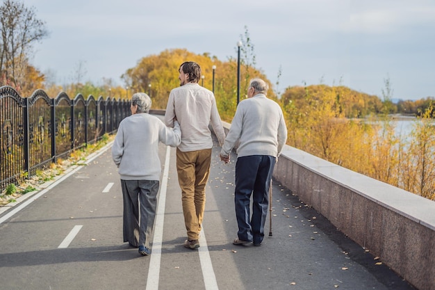 Foto um casal de idosos caminha no parque com um assistente masculino ou neto adulto cuidando do voluntariado idoso