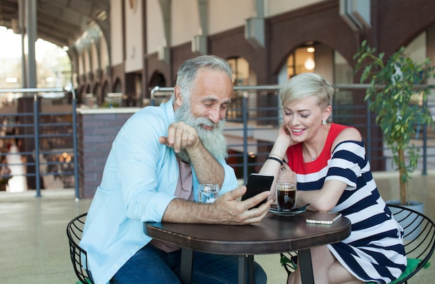 Um casal de idosos está conversando com seus filhos usando o telefone. Ela está acenando para a filha na tela.