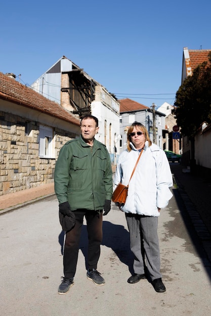 Um casal de idosos está em frente a uma casa em ruínas