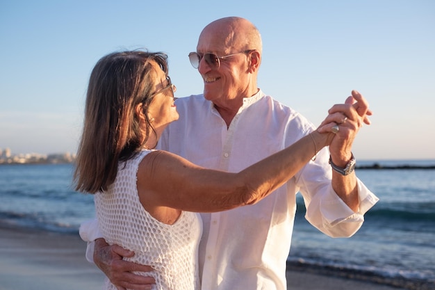 Um casal de idosos feliz a dançar na praia a desfrutar de férias e aposentadoria.