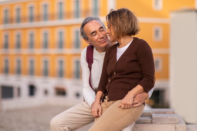 Um casal de idosos feliz a desfrutar do tempo juntos a abraçar-se sentados lá fora.