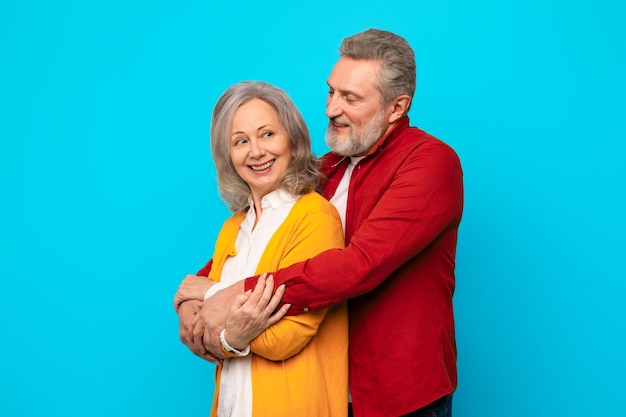 Um casal de idosos feliz e apaixonado abraçando-se com afeto contra um fundo azul.
