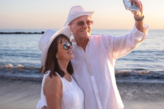 Um casal de idosos feliz na praia a desfrutar de férias e aposentadoria a fazer uma selfie com o smartphone.