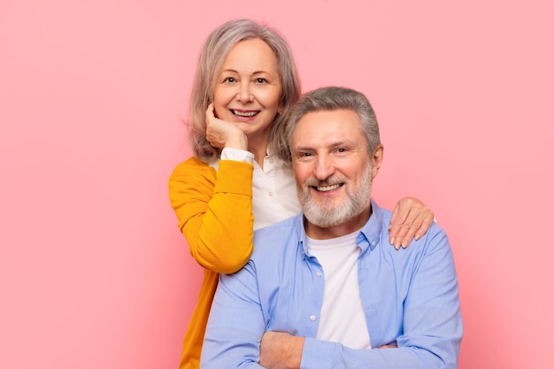 Um casal de idosos sorridente abraçando-se posando para um retrato contra um fundo rosa