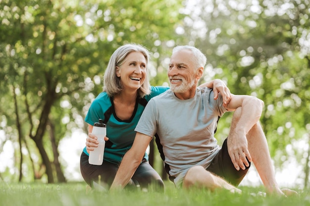 Um casal de idosos sorridente, uma mulher e um homem maduros, a relaxar juntos no parque depois de se exercitarem.