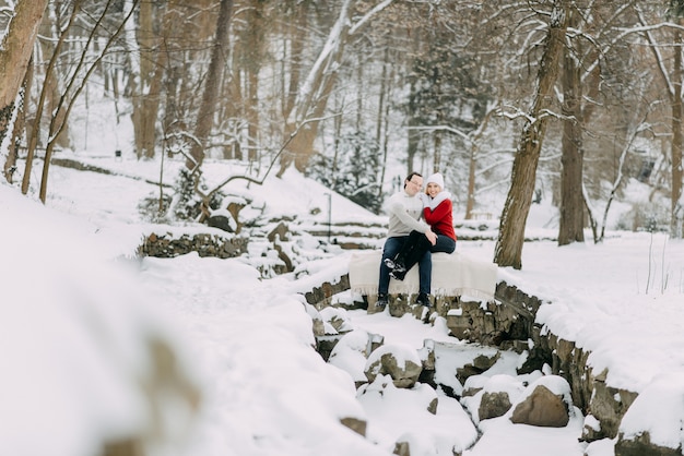 Um casal de jovens amantes em casacos de inverno e lenços, sentado em um parque de neve