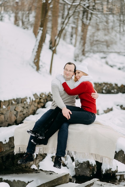 Um casal de jovens amantes em casacos de inverno e lenços, sentado em um parque de neve