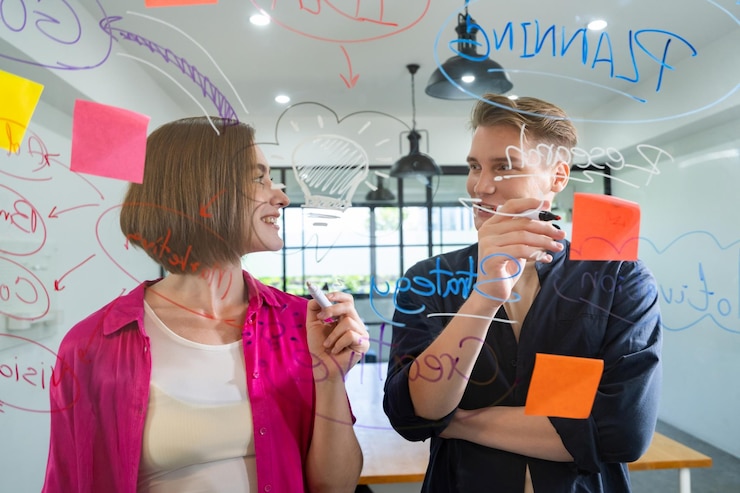 Foto um casal de jovens empresários criativos a fazer brainstorming de ideias e a resolver problemas usando notas adesivas e mapas mentais na sala de reuniões do tabuleiro de vidro a discutir o trabalho em conjunto.