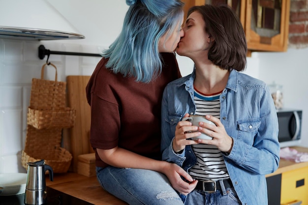 Um casal de lésbicas a beijar-se na cozinha de manhã.