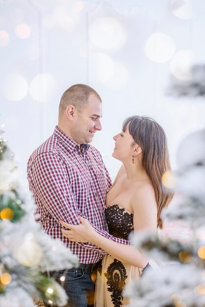 Um casal de meia-idade com roupas elegantes contra uma árvore de natal com neve