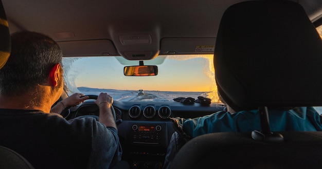 Um casal de meia-idade dirigindo um 4x4 de dentro do carro ao amanhecer em uma estrada totalmente nevada sol nascendo