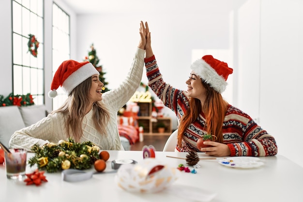 Um casal de mulheres fazendo decoração de Natal feita à mão com as mãos erguidas em casa.