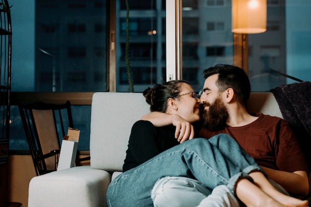 Um casal de namorados se olhando no sofá com amor enquanto tocam o nariz com o espaço da cópia